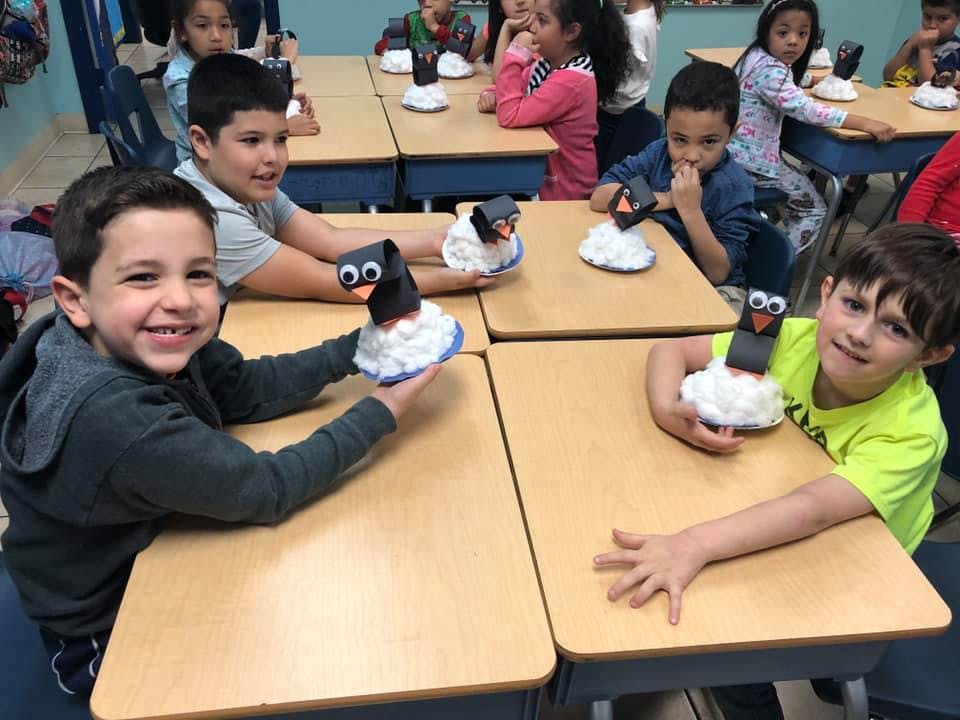 Children in a classroom holding penguin crafts