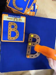 Child's hand holding a tool to assemble a letter B puzzle