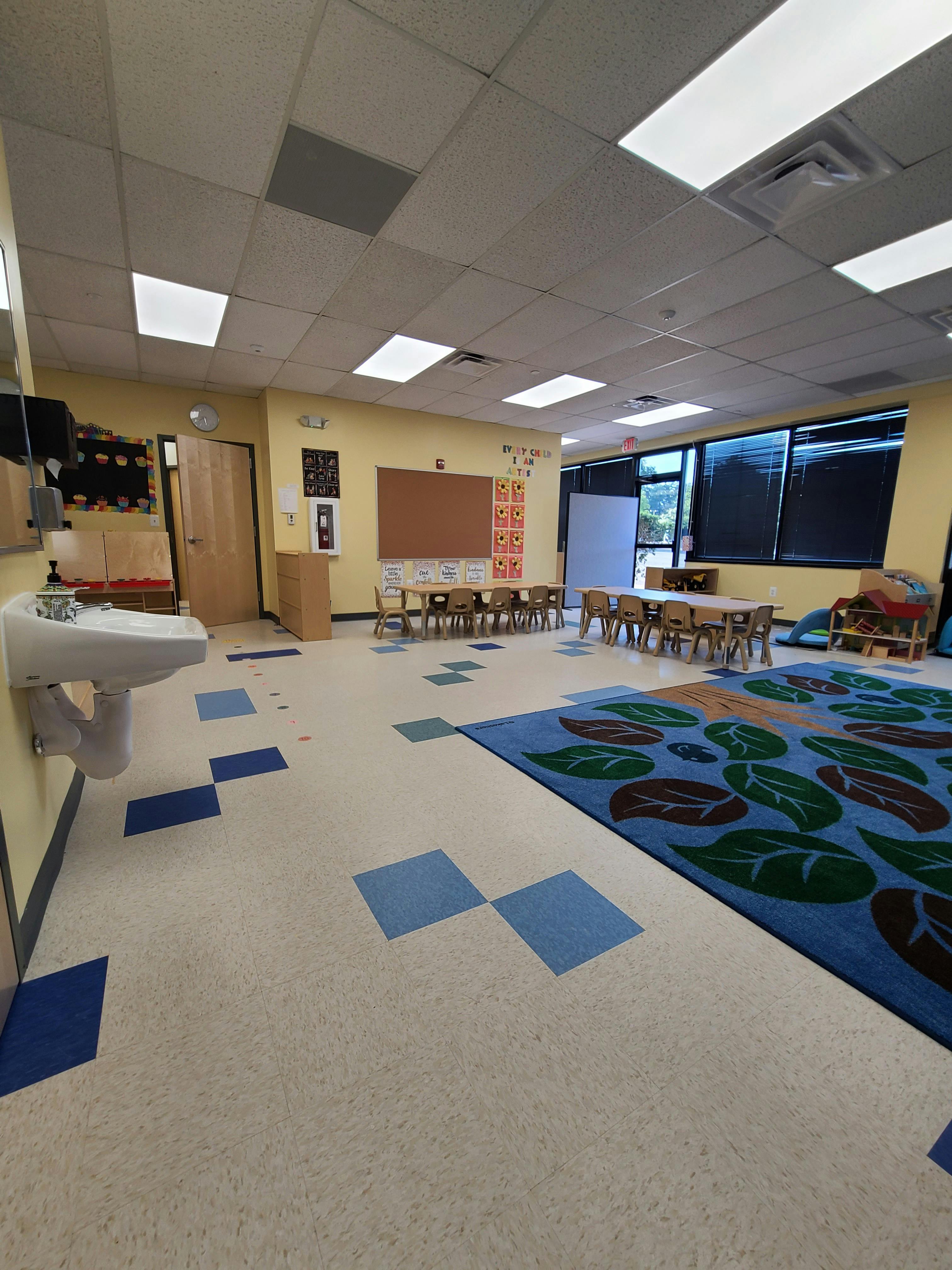 Classroom with small tables and chairs, a sink, and a blue rug