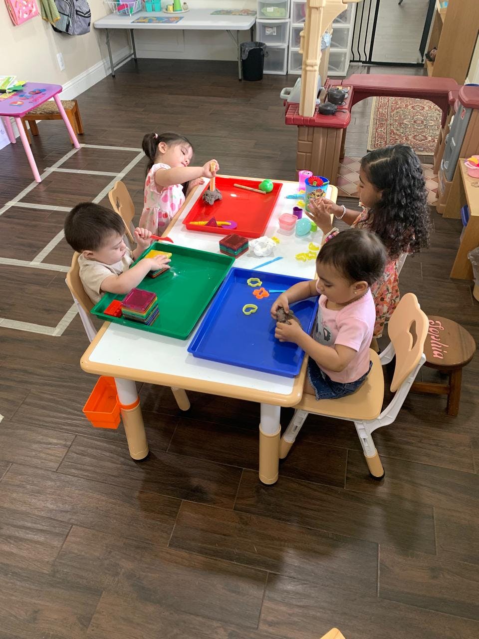 Four children at a table playing with colorful trays and objects