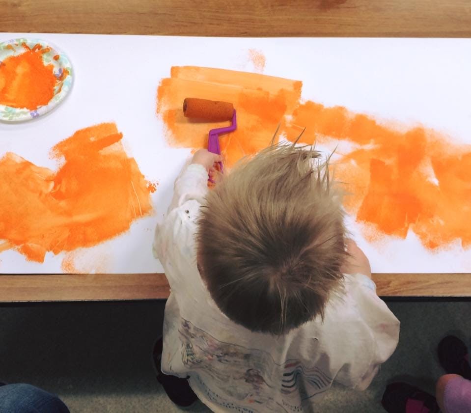 Child painting with an orange roller