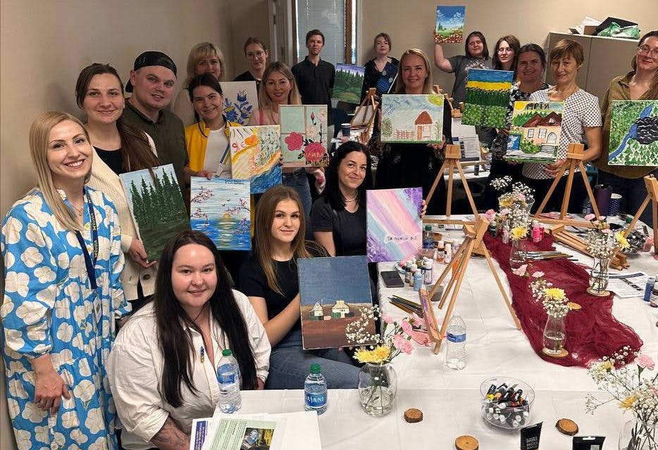 Group of people holding up paintings from an art class