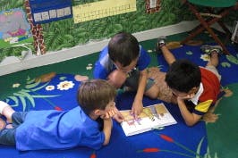Three children lying on a rug looking at a book