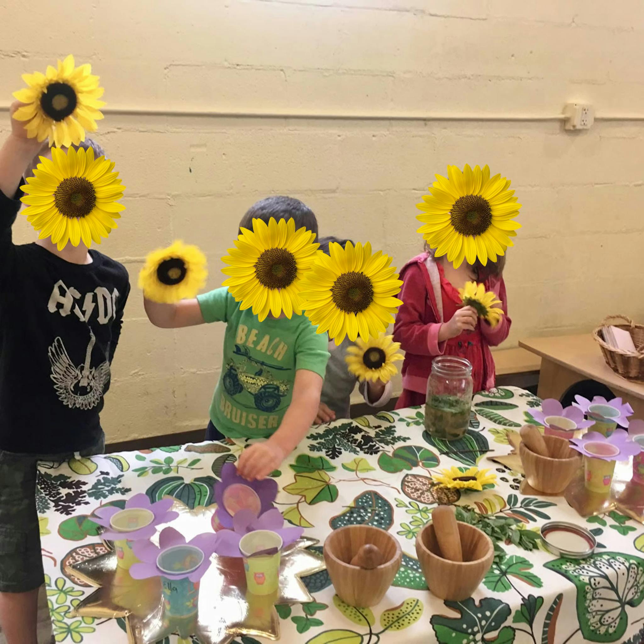 Several children holding sunflowers and interacting with crafts on a patterned tablecloth