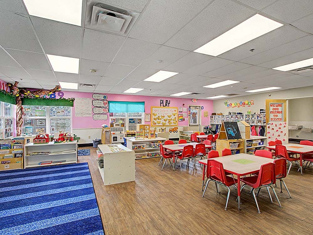 Classroom with small red tables and chairs, play kitchen, and books