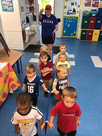 Person in Texas shirt leading a line of children holding a blue ribbon