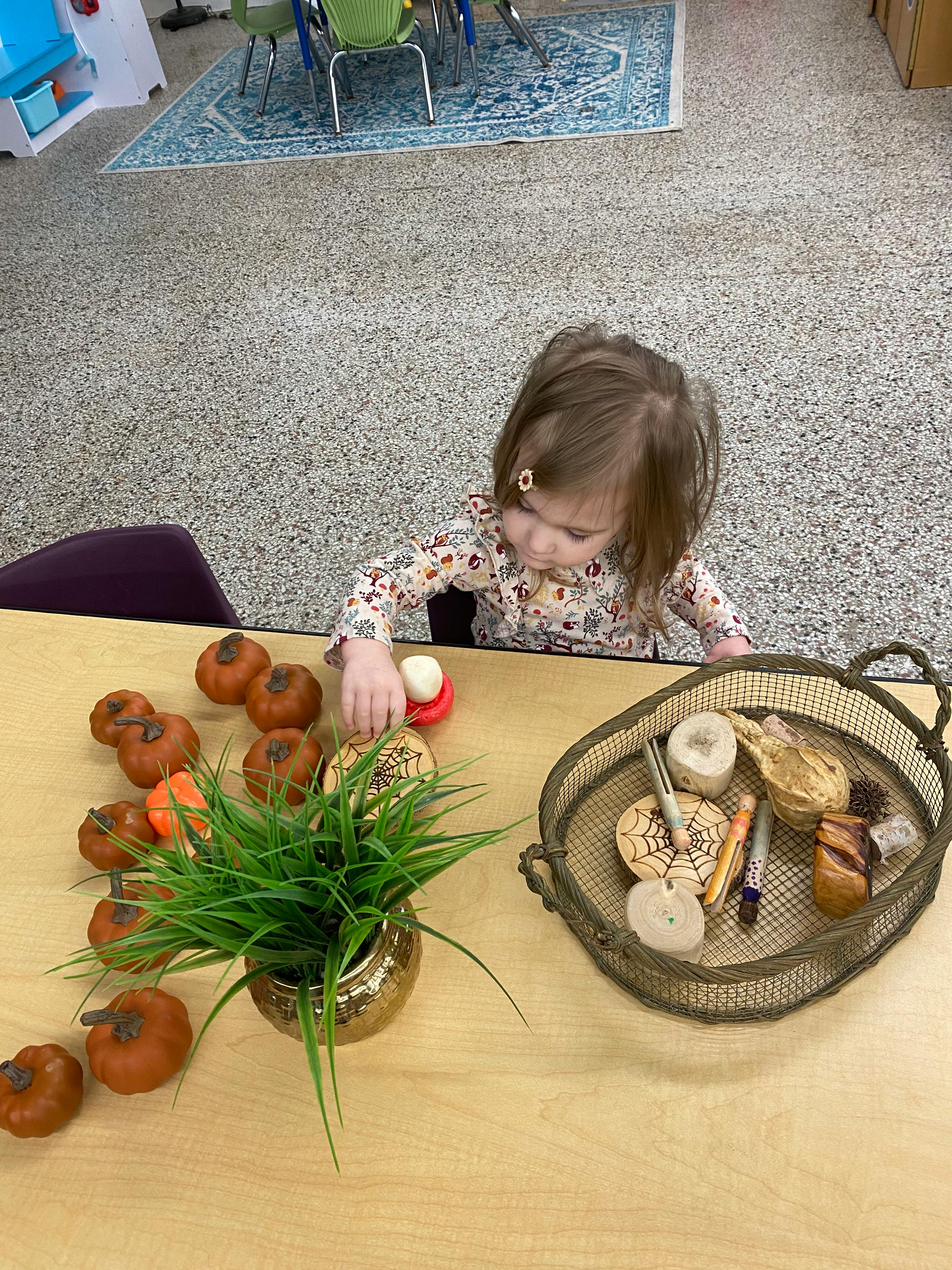 Child playing with small pumpkins and a basket of craft items on a table