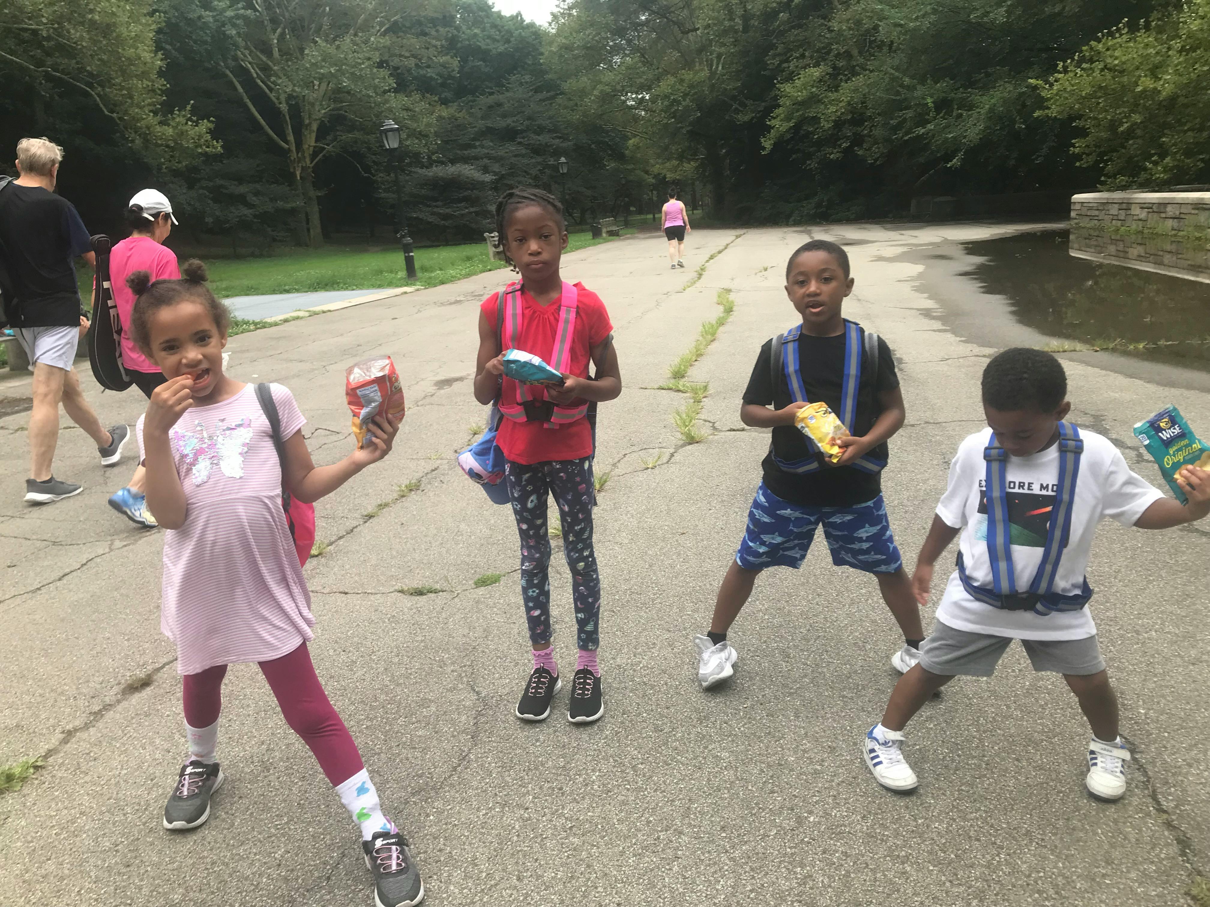 Four children standing on a paved path, three holding snacks