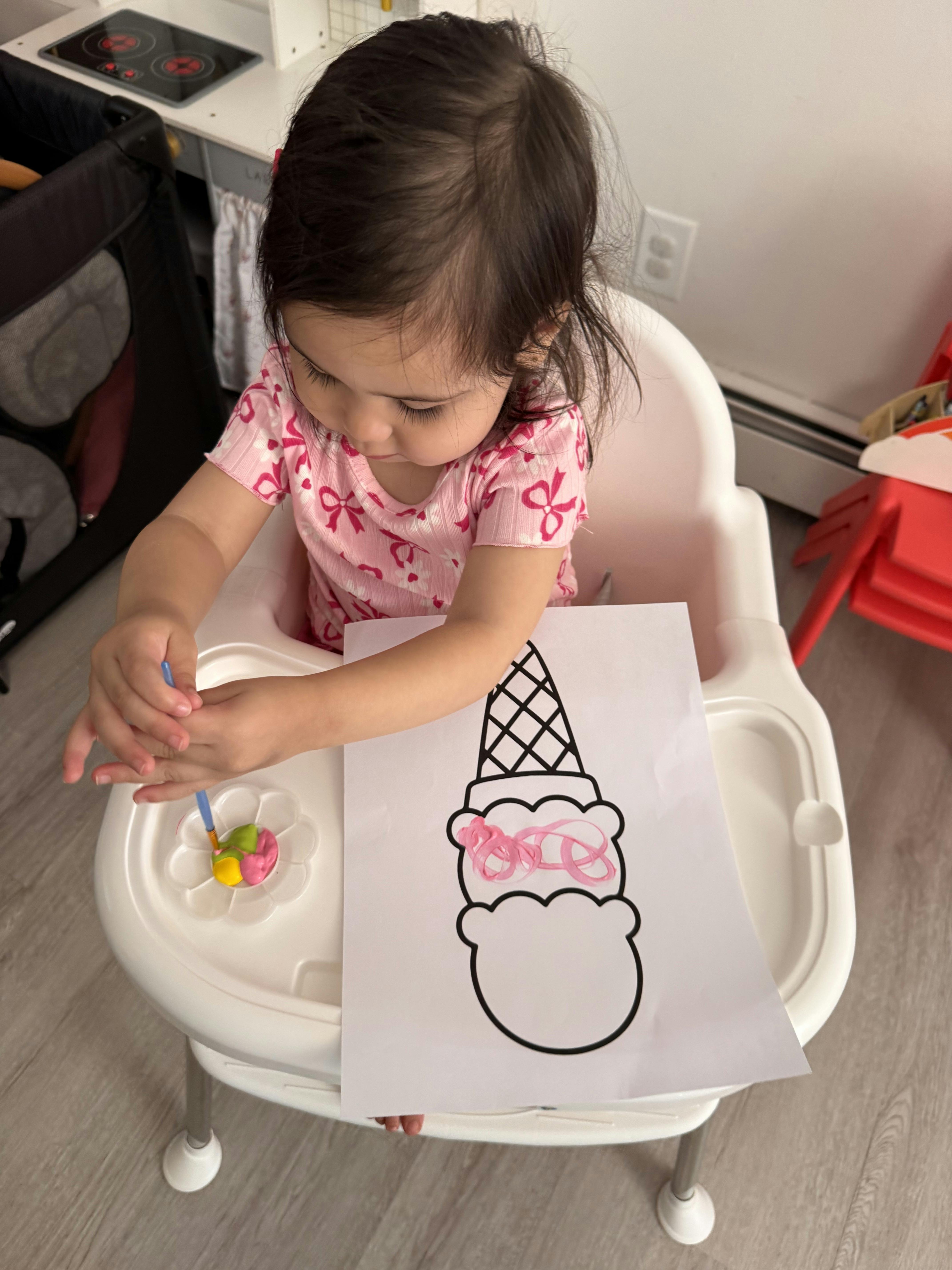 Child sitting in a high chair painting an ice cream drawing