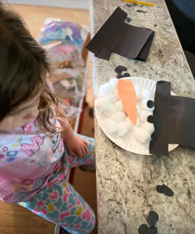 Child looking at a paper plate craft with cotton balls and paper cut paper