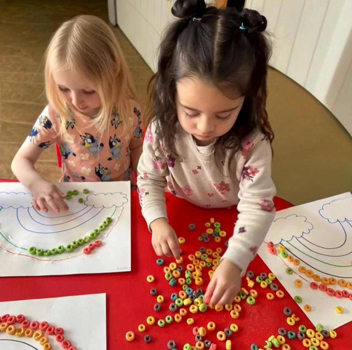 Two children making rainbows with colorful cereal pieces on paper