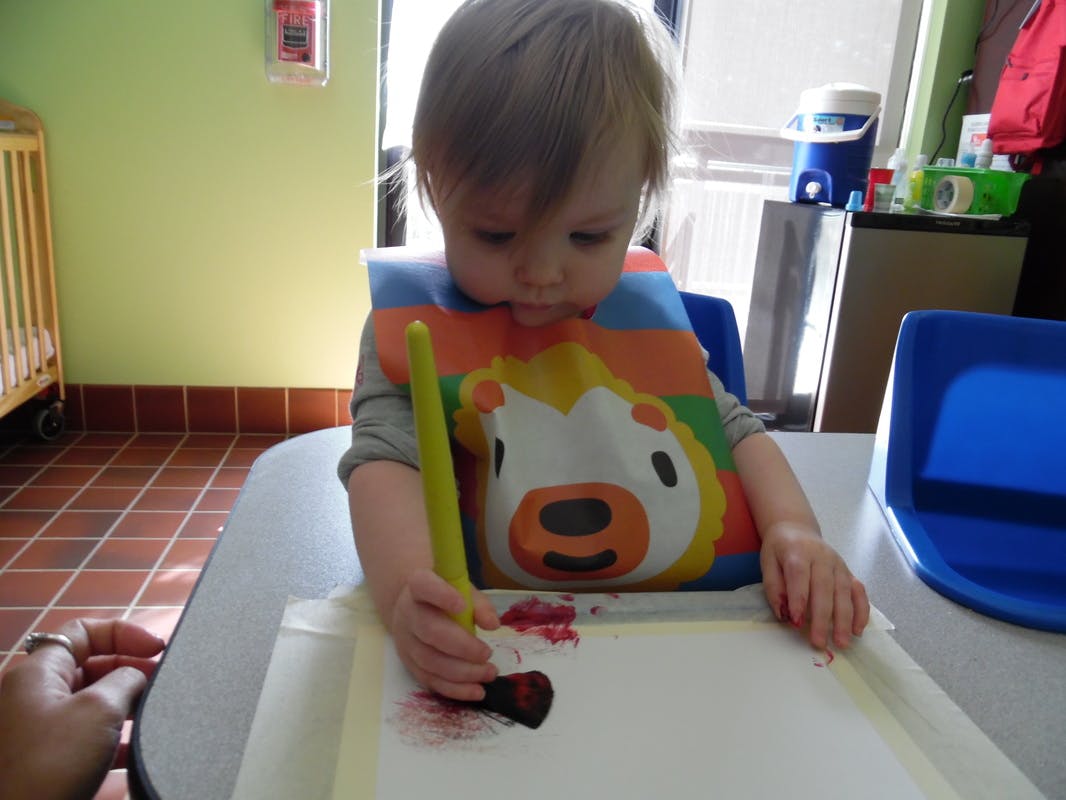 Child in a bib painting on paper with a brush
