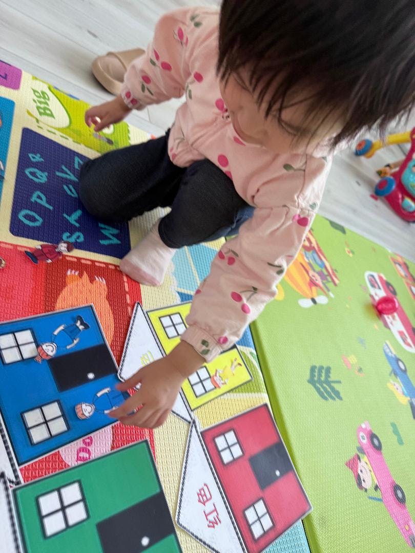 Child playing with colorful house-shaped puzzle pieces on a mat