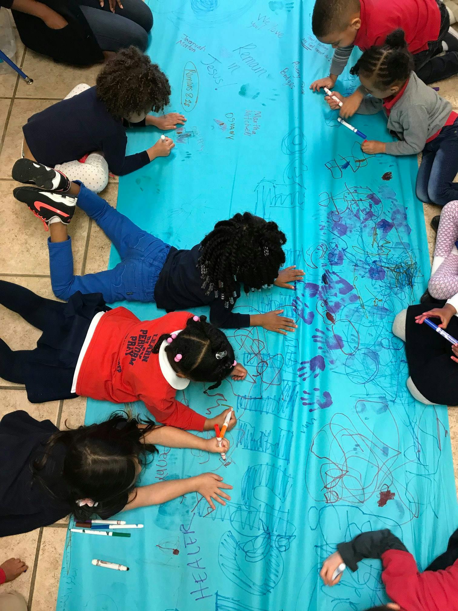 Children drawing on a long blue sheet on the floor