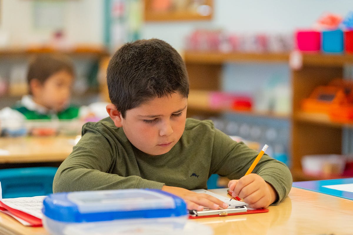Child writing on a clipboard in a classroom