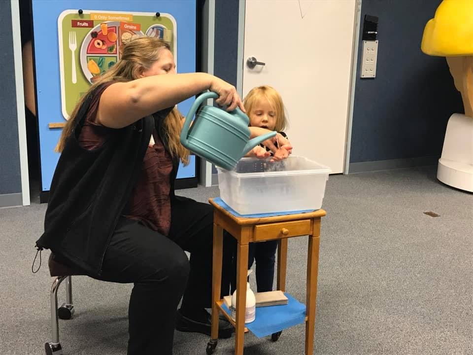 Person pouring water from a watering can into a bin for a child