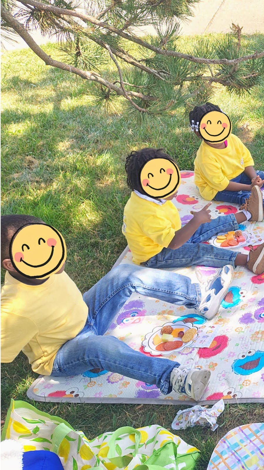 Three children sitting on a picnic mat on the grass eating snacks