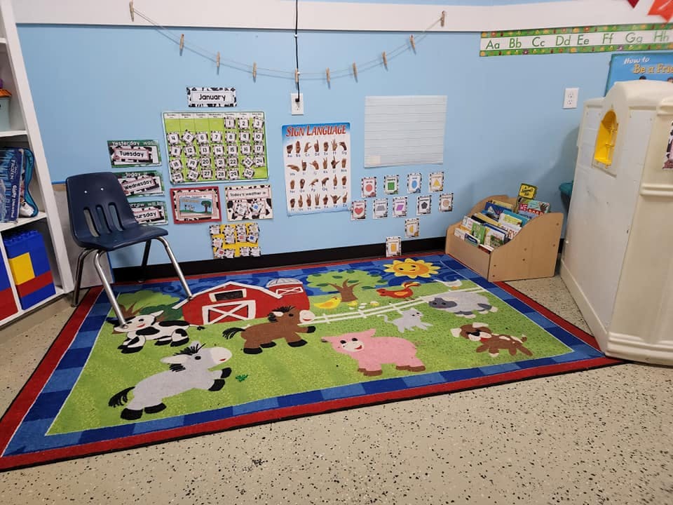 Classroom with a farm animal rug, blue chair, and educational posters