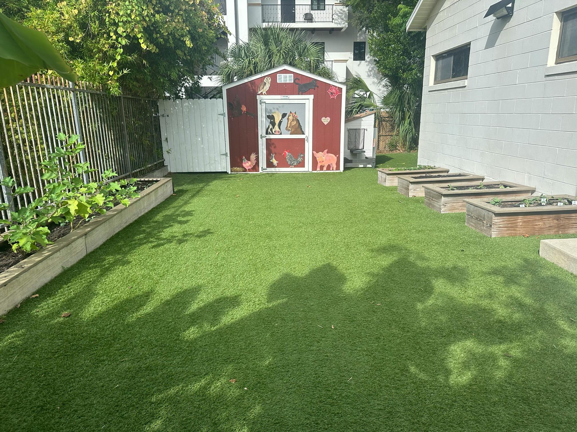 Red playhouse in a grassy backyard with raised garden beds