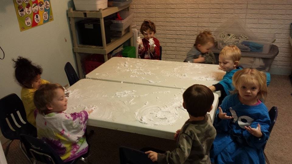 Children sitting around a table covered in white powder