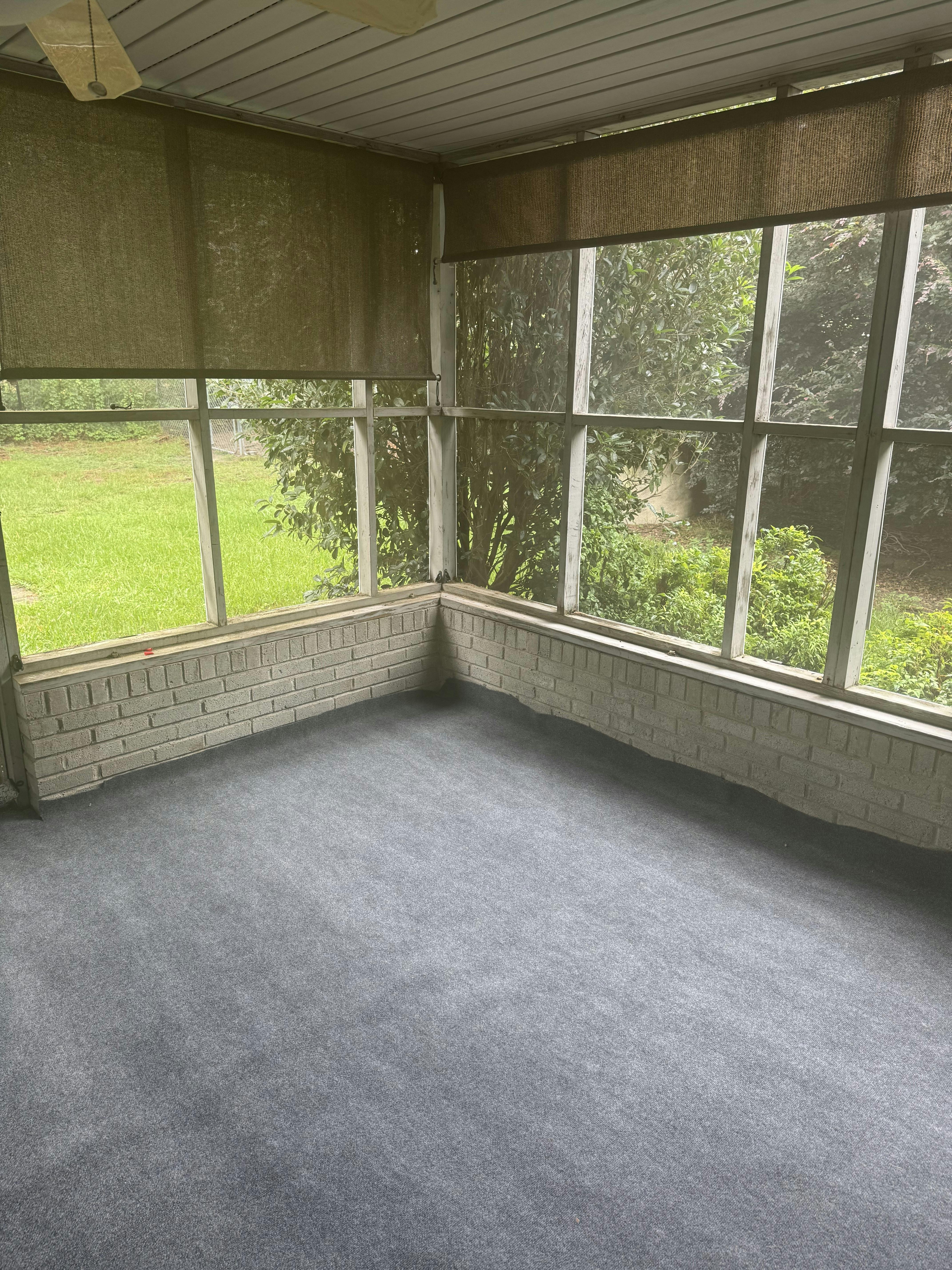 Empty screened-in porch with a view of green grass and trees