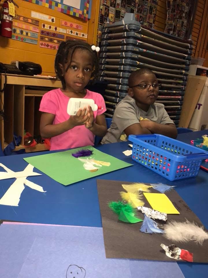 Child holding glue bottle at a table with craft supplies