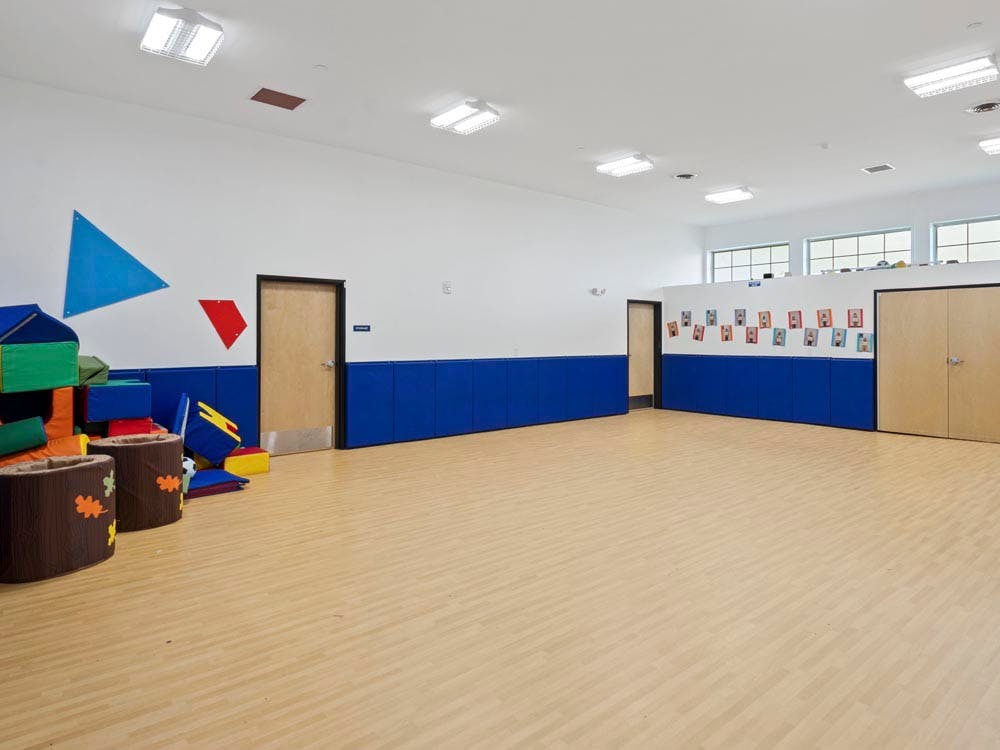Empty classroom with light wooden floor, blue wainscoting, and colorful soft blocks