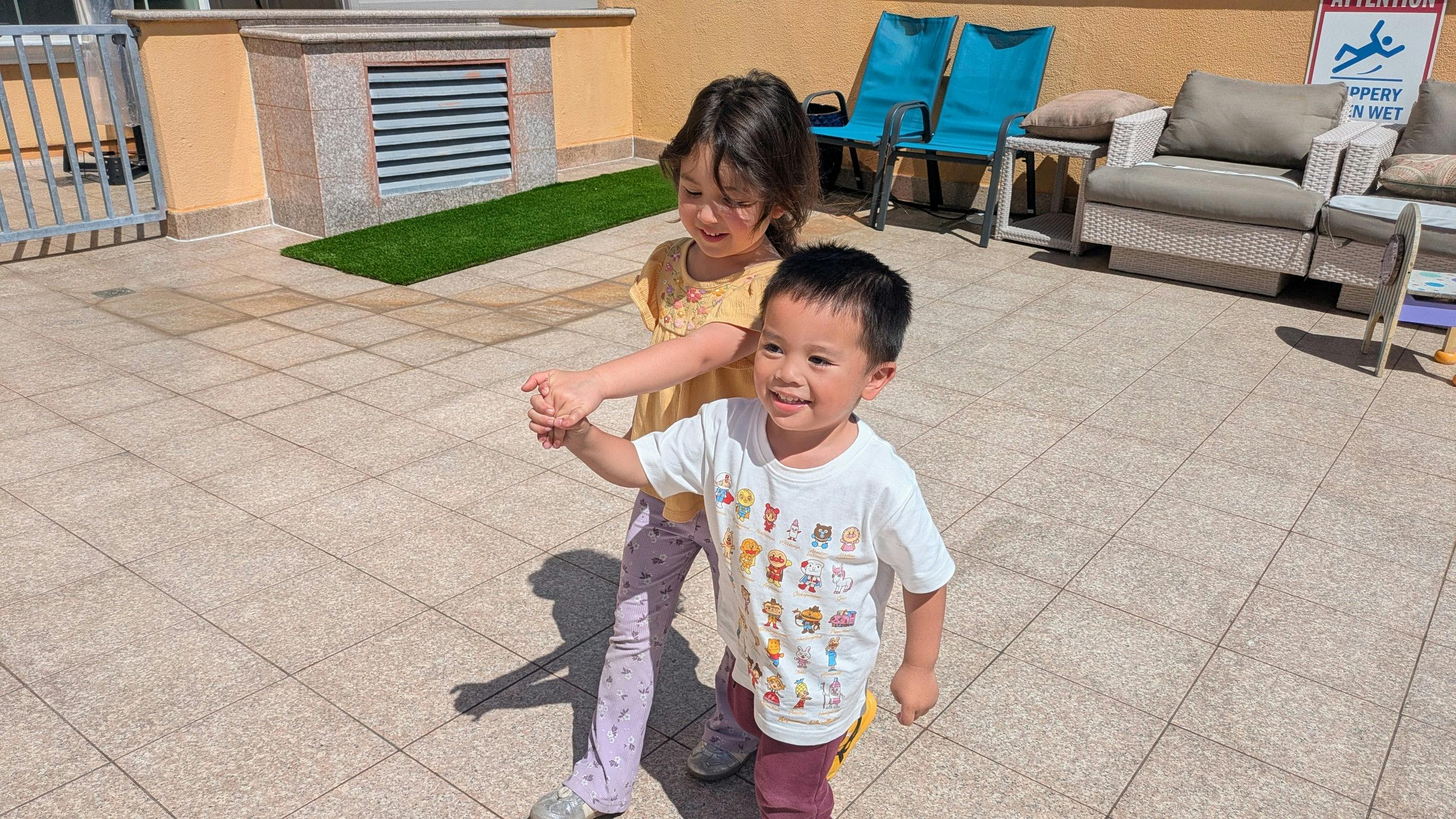 Two children holding hands while walking on a patio