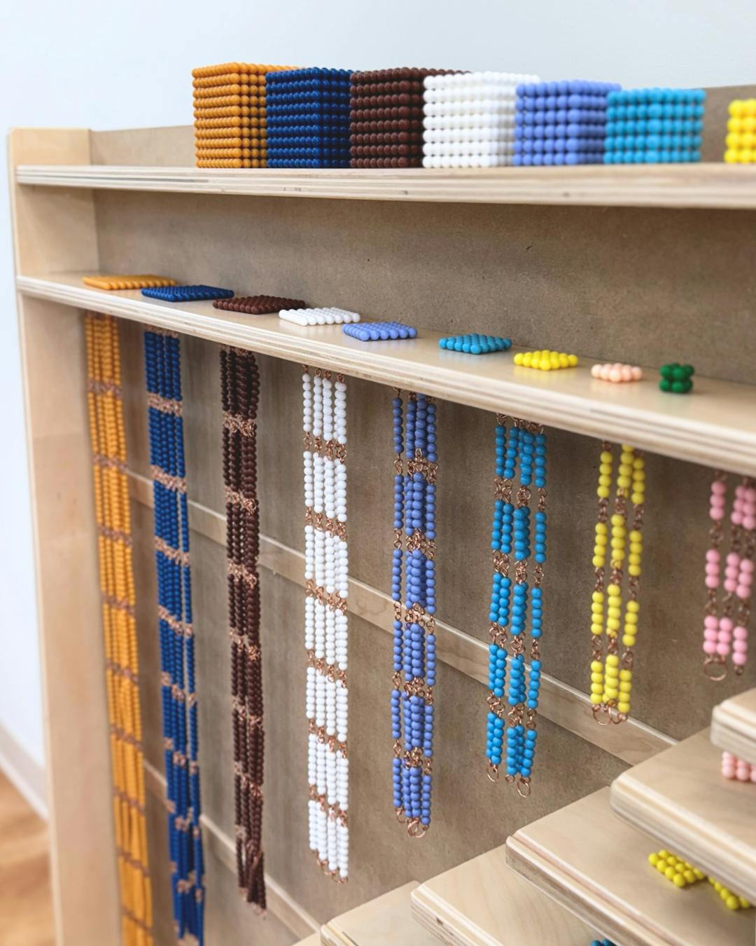 Colorful Montessori bead chains and cubes on wooden shelves