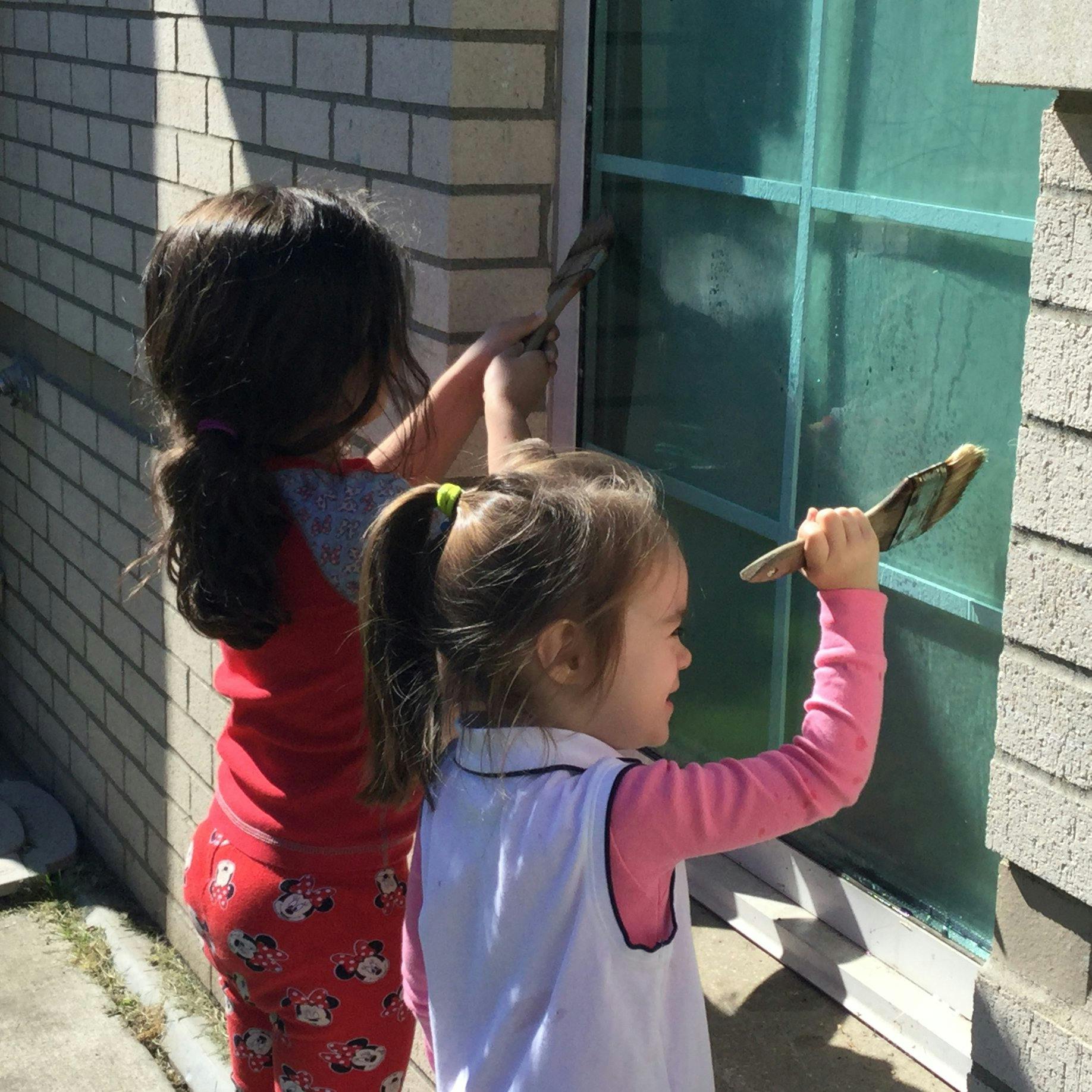 Two children painting a window