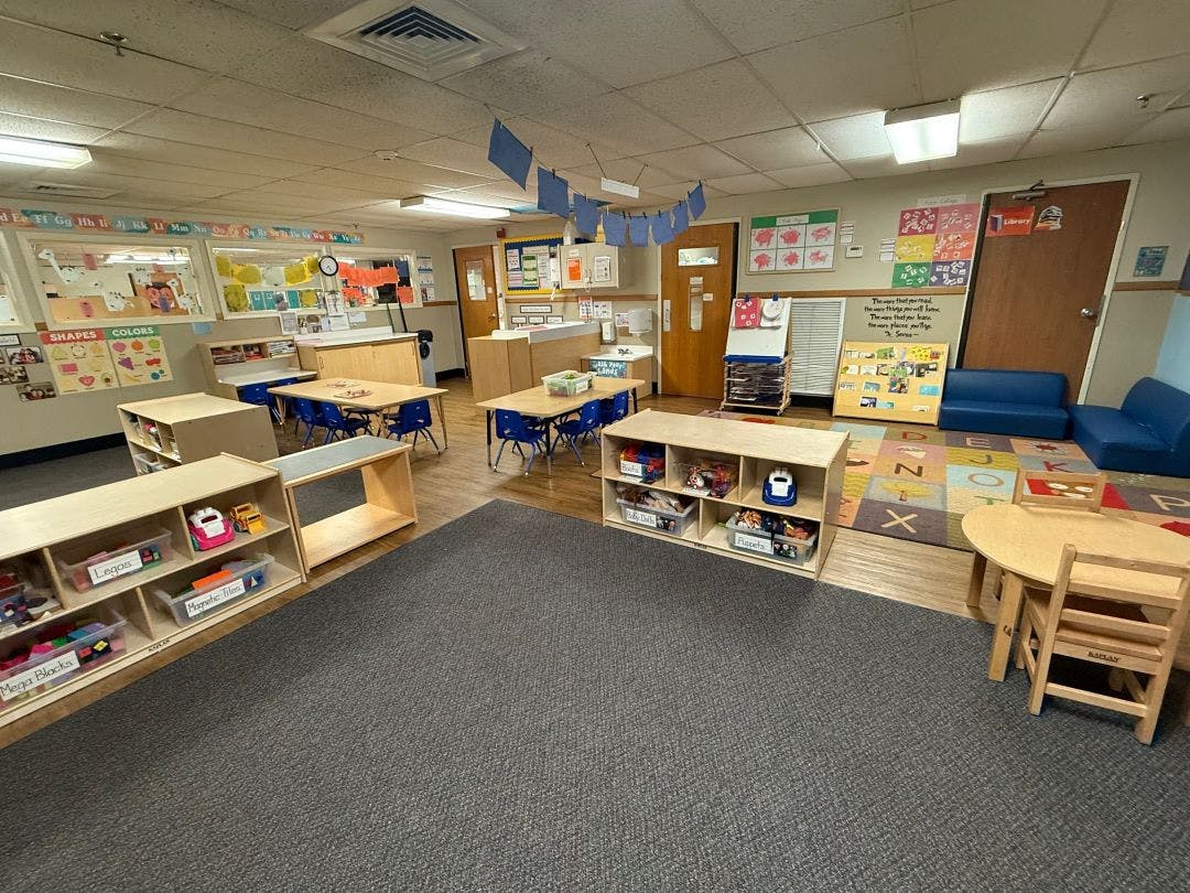 empty preschool classroom with tables, chairs, and shelves of toys