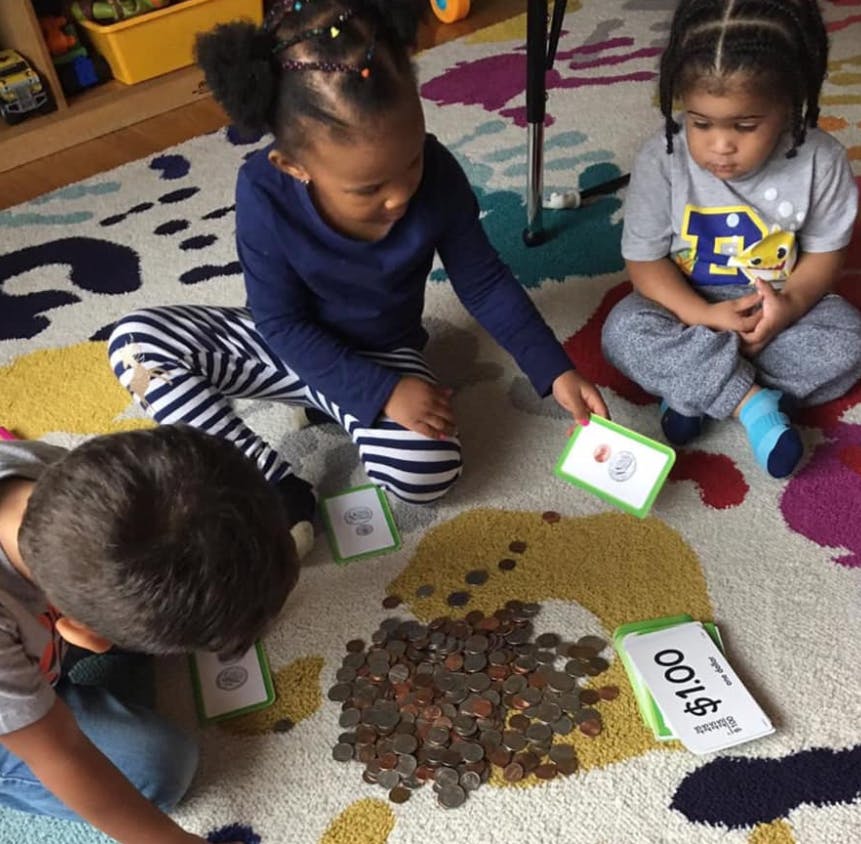 Three children playing with coins and cards on a rug