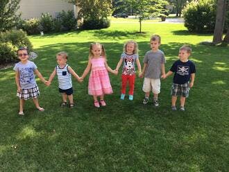 Six children holding hands in a line on grass