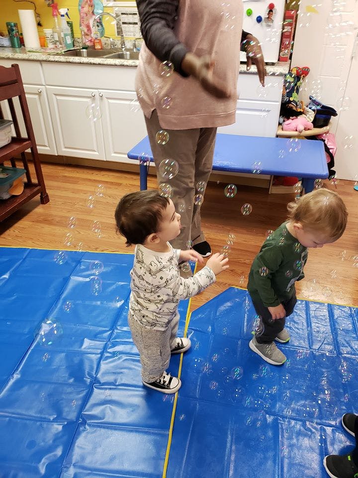 Two children playing with bubbles on a blue mat, with a person standing nearby