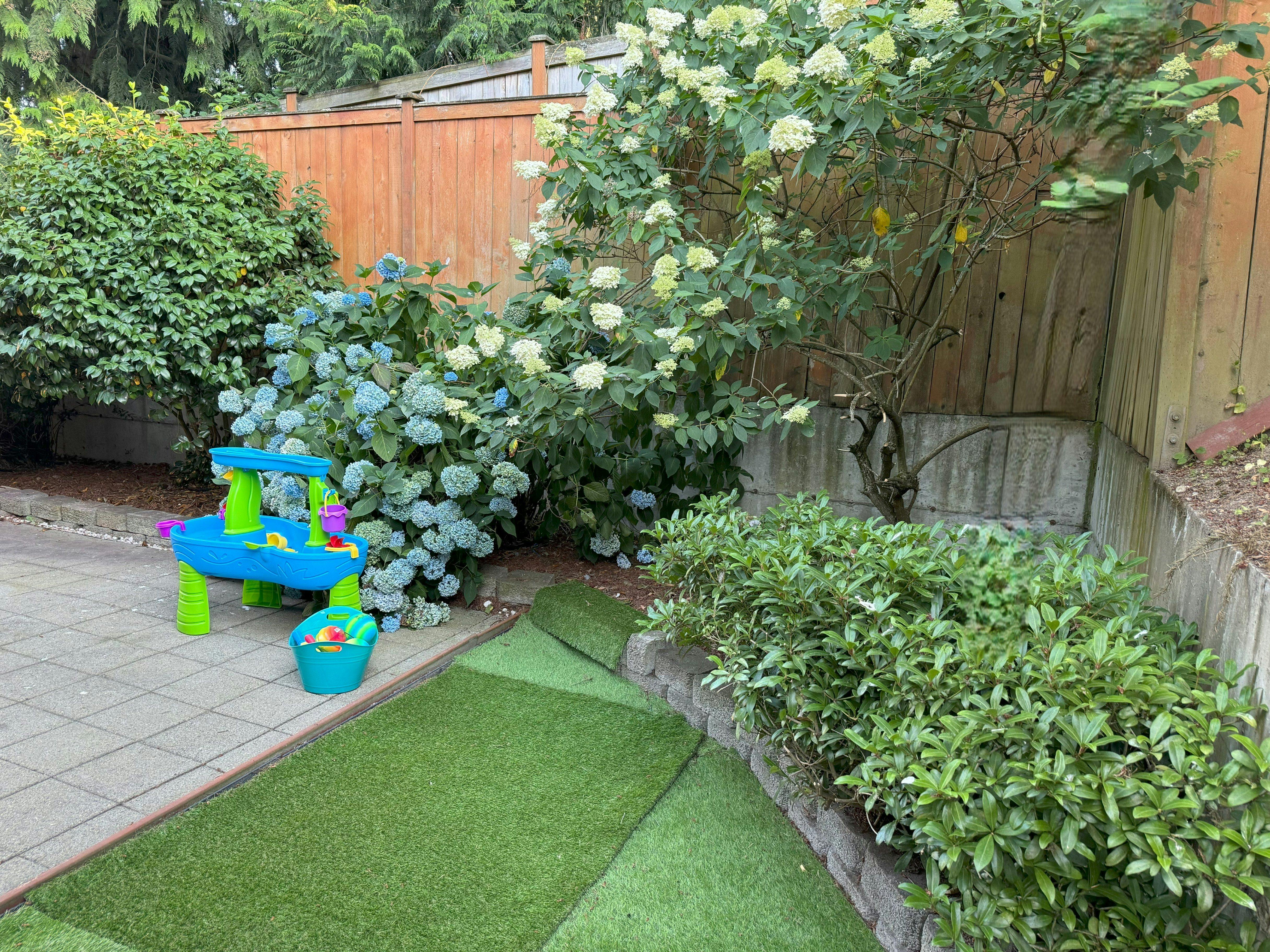 Blue and green play table on a patio next to bushes and a wooden fence