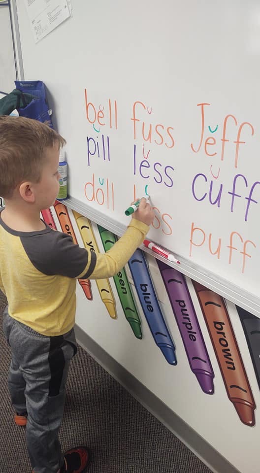 Child writing words on a whiteboard with a marker