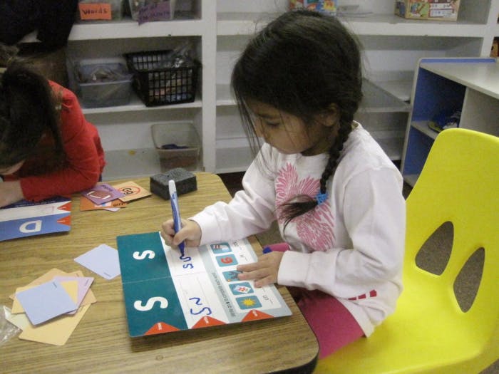 Child writing on a workbook at a table in a classroom