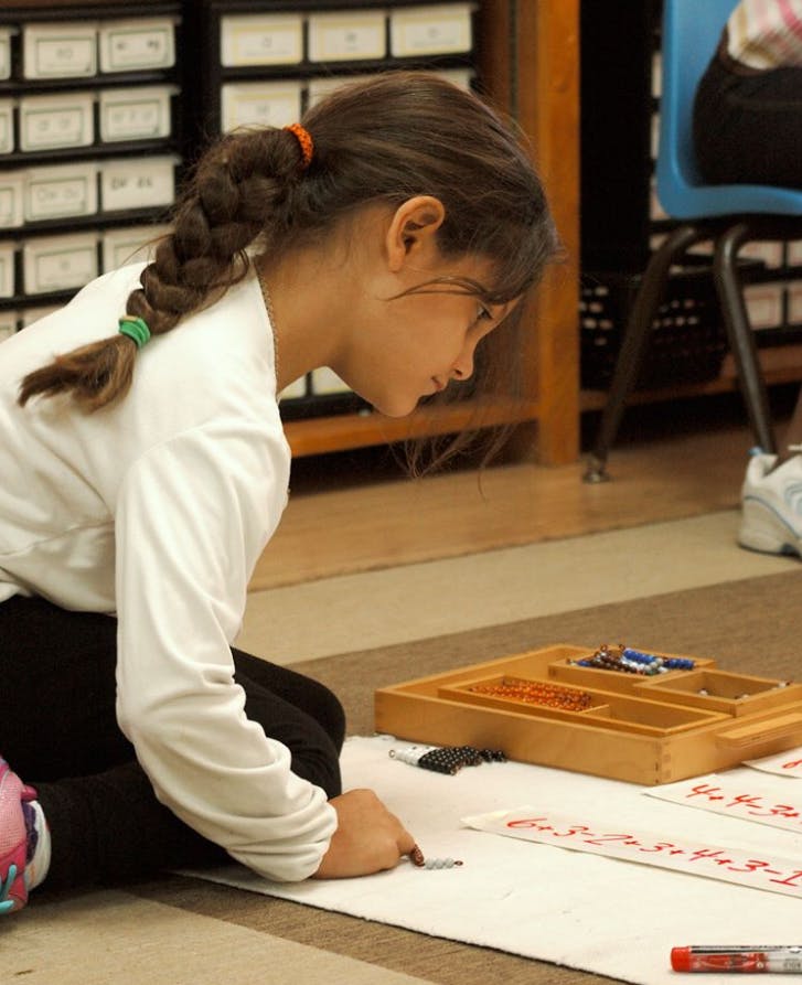 Child kneeling on floor, writing on paper with a pen