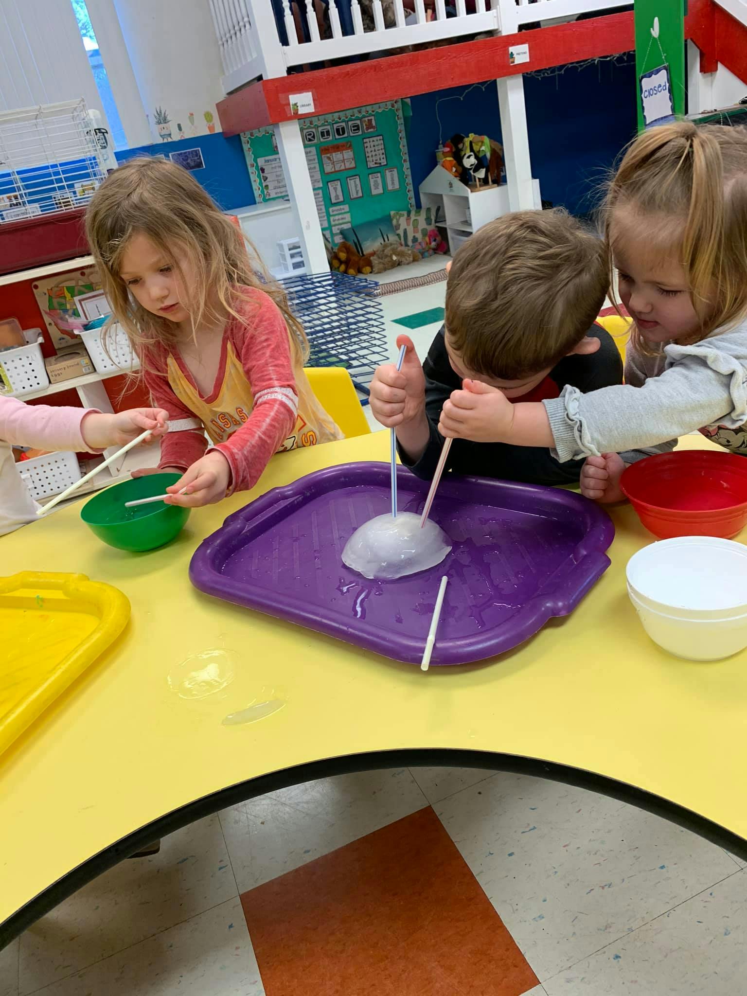 Three children at a table playing with straws and bowls