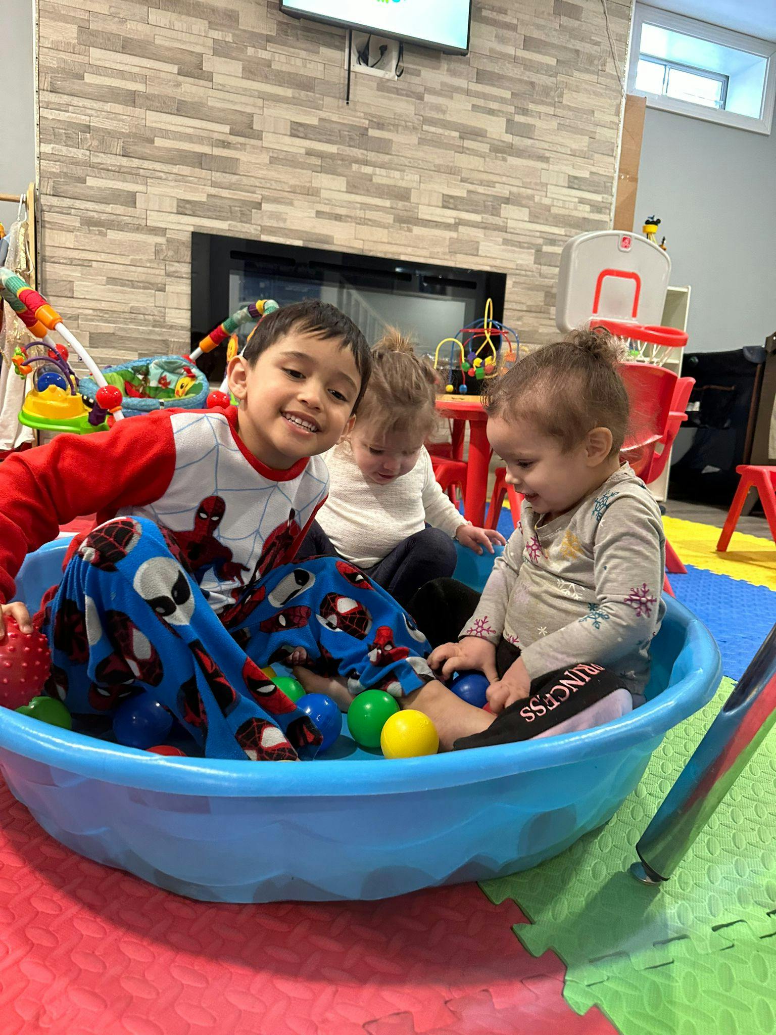 Three children playing in a blue plastic pool with colorful balls