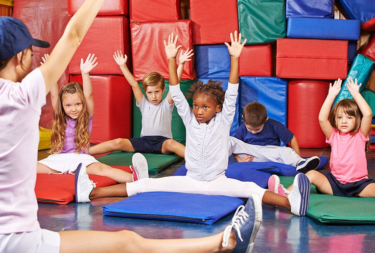 Children stretching with arms raised in a gym class