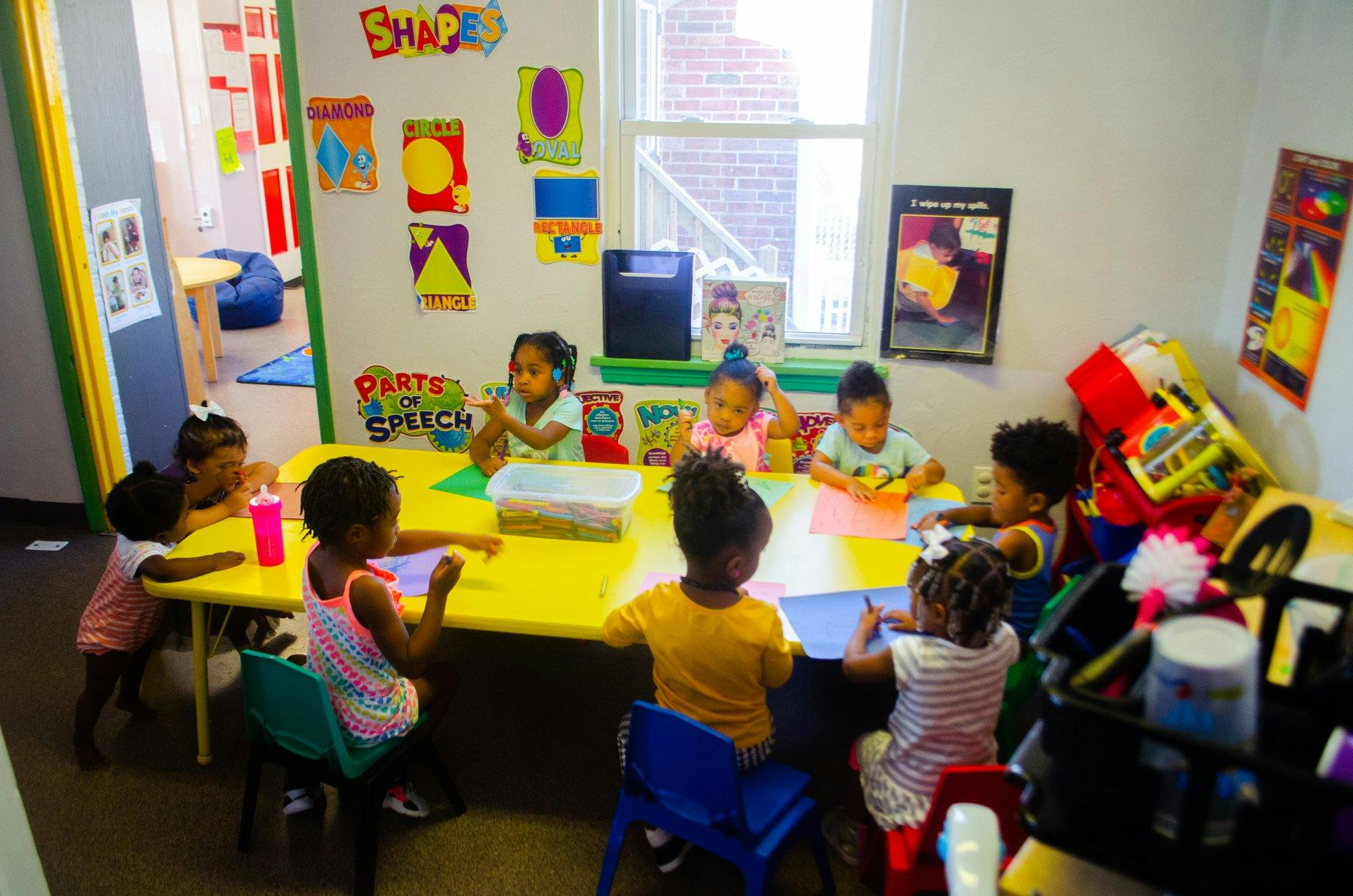Children sitting at a yellow table in a classroom