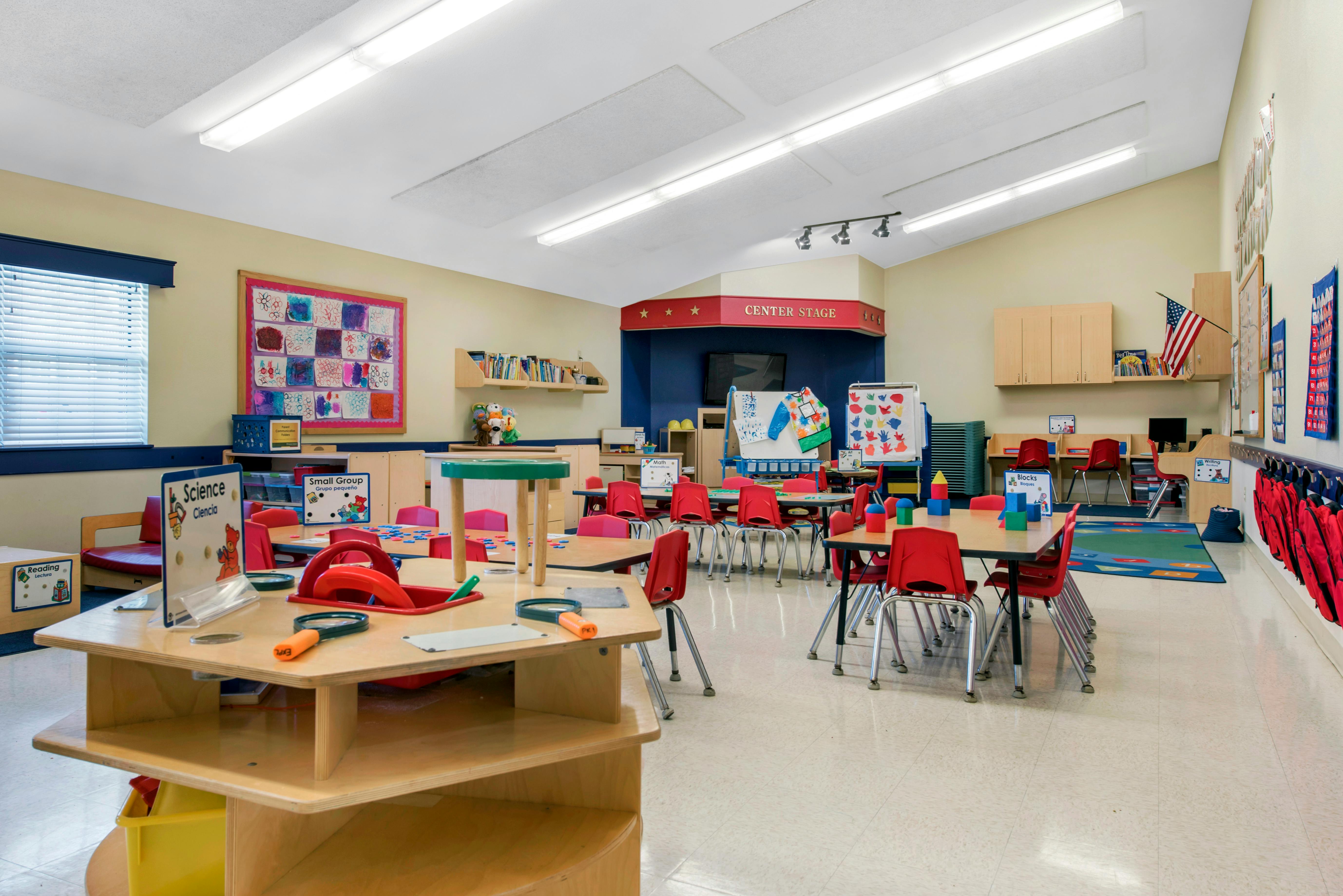 An empty early childhood classroom with multiple small tables and red chairs