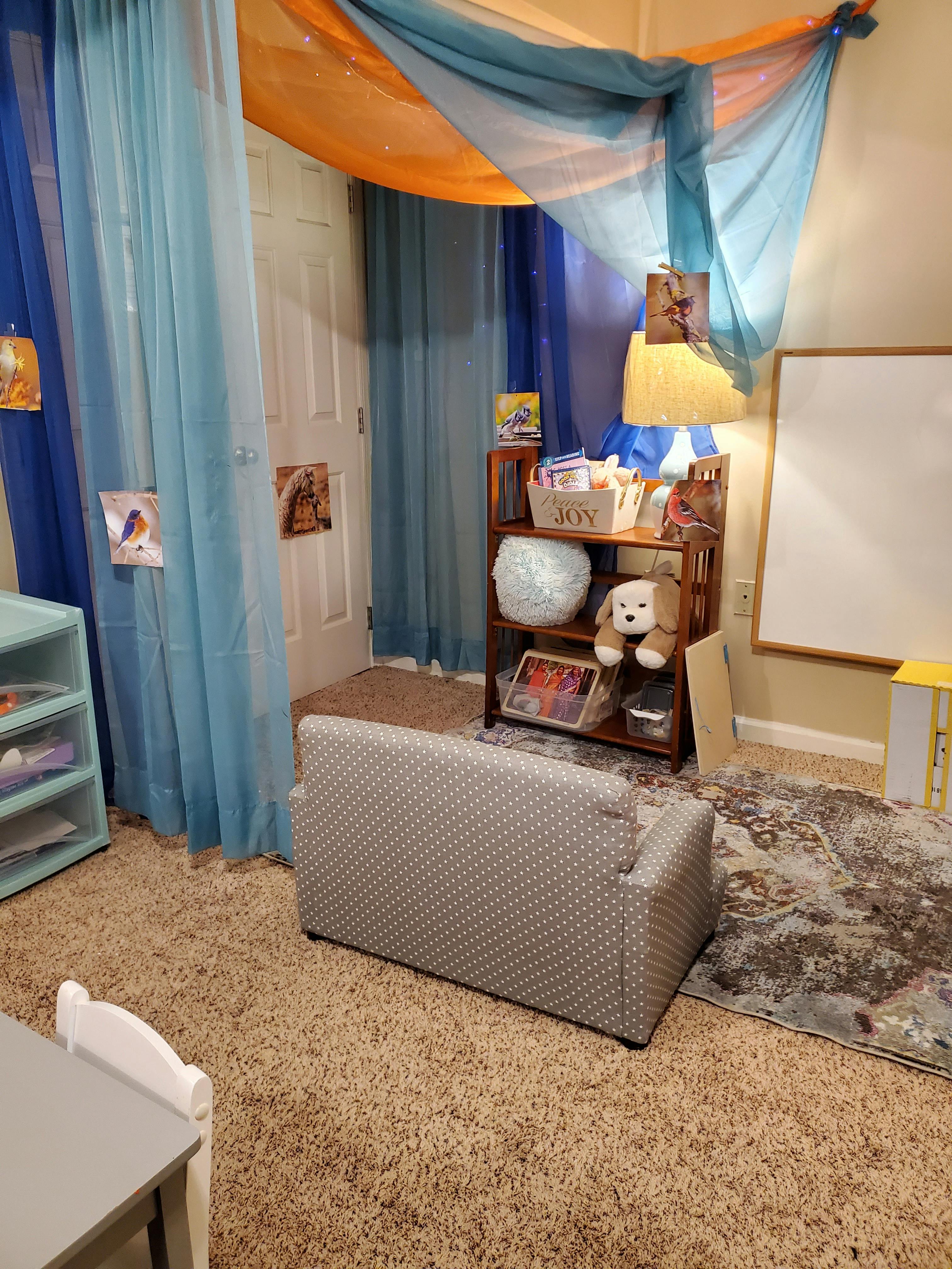 Room with a small sofa, bookshelf, and sheer blue and orange fabric draped from the ceiling