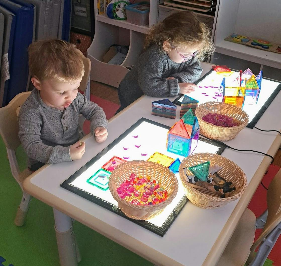 Two children playing with colorful magnetic tiles on light tables
