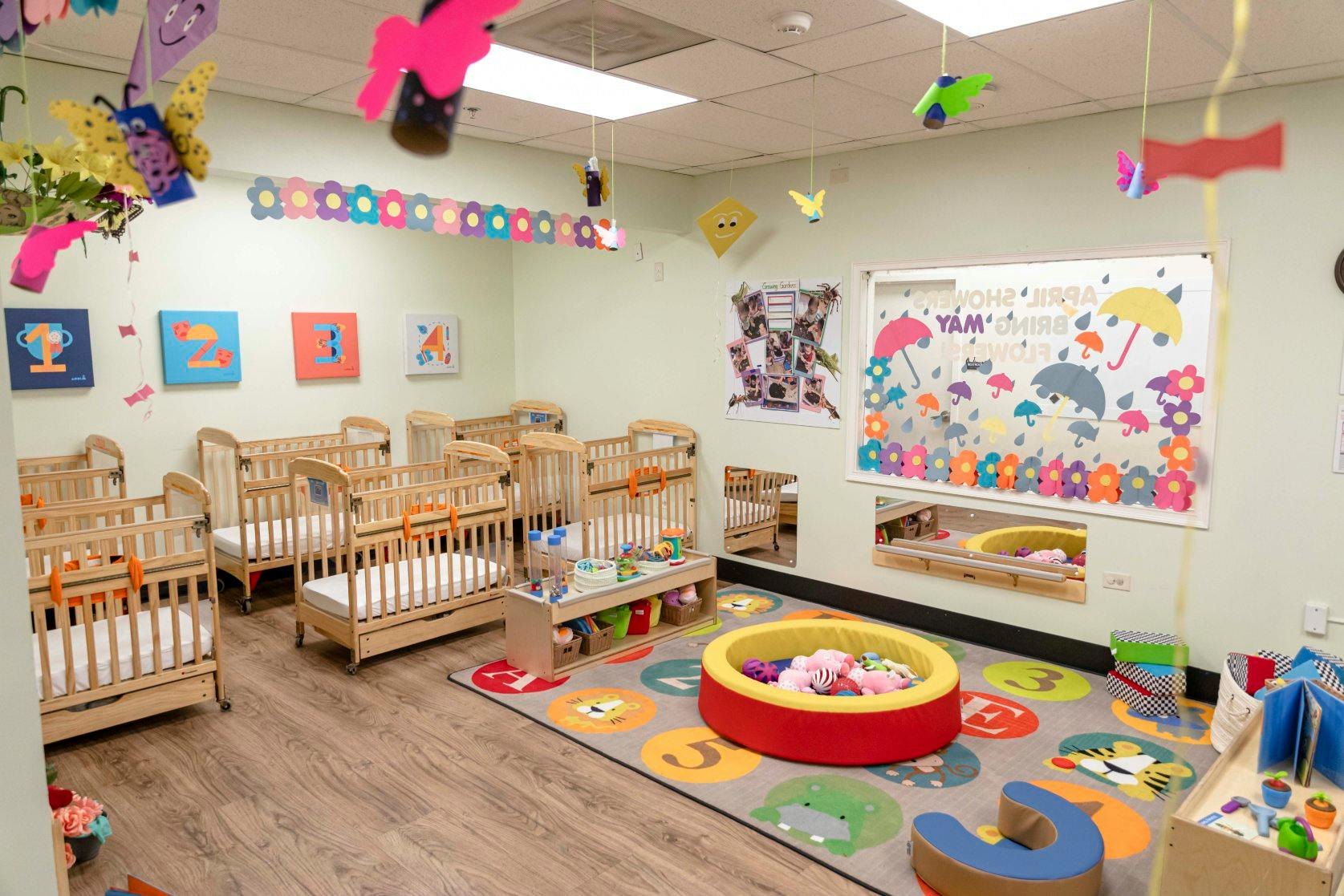 A room with multiple cribs, a play mat, and toys