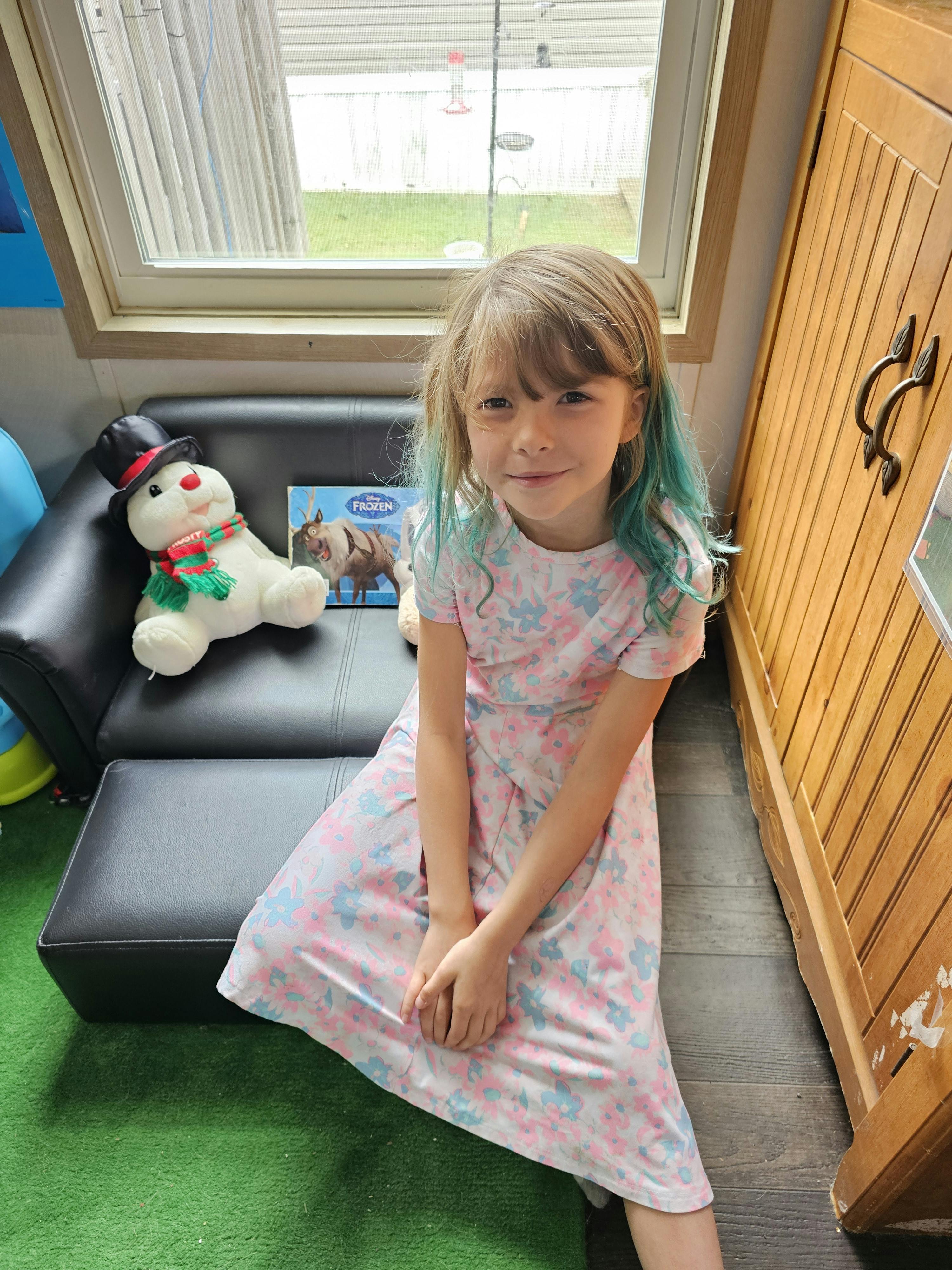 Child with blue-tipped hair sitting on the floor next to a black couch