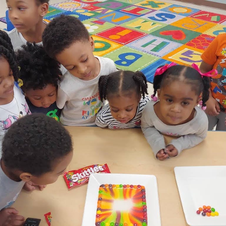 Children gathered around a table looking at a colorful square cake