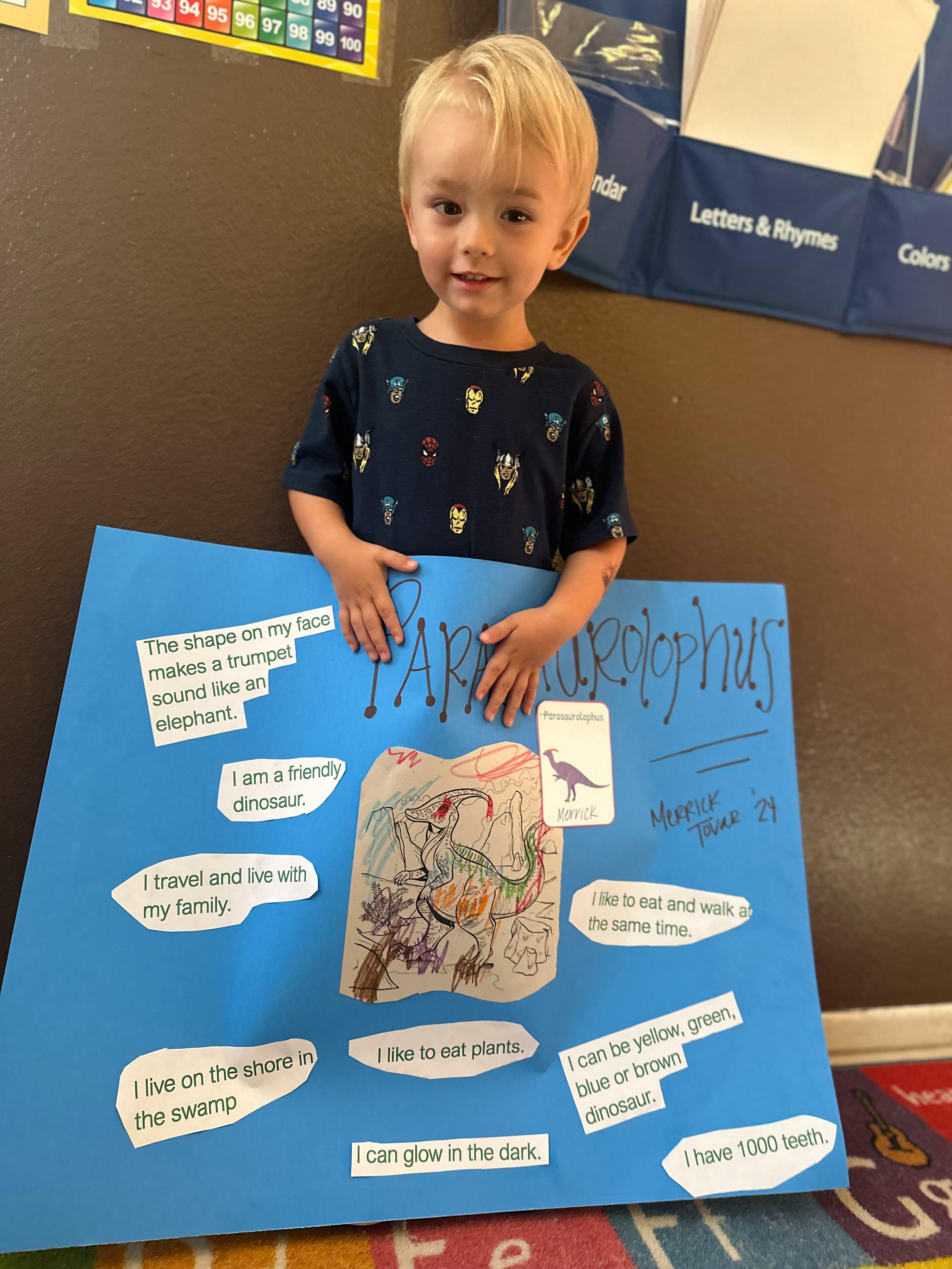 Child holding up a blue poster board with text and drawings about a dinosaur
