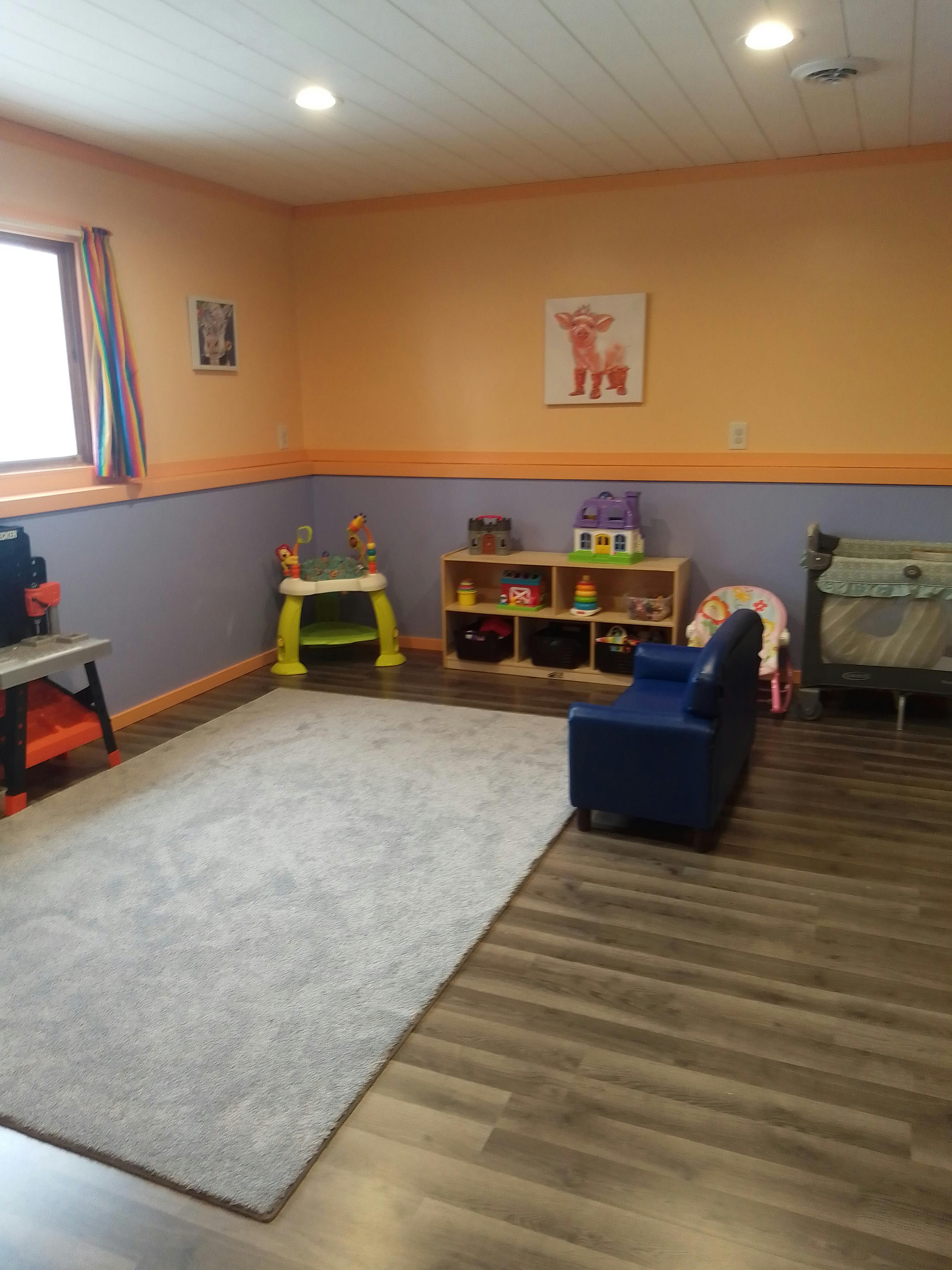 Playroom with rug, small blue chair, and toys on the right a crib
